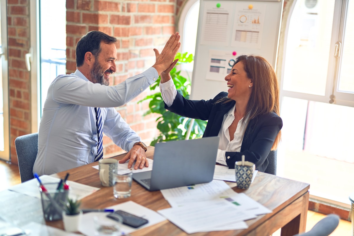 Twee collega's geven elkaar een high five aan een bureau